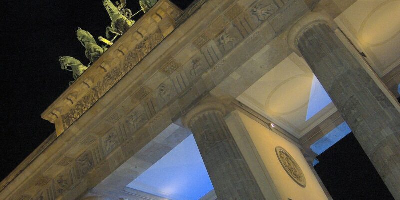 Niedrige Ansicht des Brandenburger Tors bei Nacht, beleuchtet. Die Quadriga-Statue auf dem Tor ist sichtbar, zusammen mit architektonischen Details und Säulen. Oft mit dem Berliner Tor verwechselt, leuchtet seine Pracht vor dem dunklen Himmel und hebt die beleuchteten Elemente des Tors hervor.