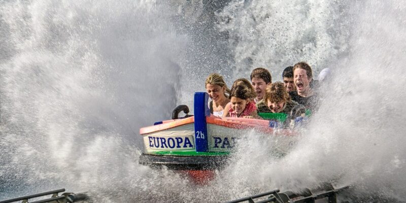 Im Europa-Park in Rust erlebt eine Gruppe bei einer aufregenden Bootsfahrt eine aufregende Kaskade von Wasser. Während das Boot einen steilen Abhang hinunterstürzt, überrollt eine heftige Welle die Passagiere, die sich festhalten und mit Aufregung und Überraschung auf das Wasserwunder des Europa-Parks reagieren.