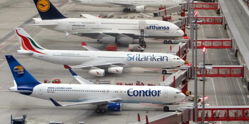 Eine Miniatur-Flughafenszene, die im Miniatur Wunderland aufgenommen wurde, zeigt Modellflugzeuge von Fluggesellschaften wie Condor, SriLankan und Lufthansa. Diese Flugzeuge parken an Gates mit angeschlossenen Fluggastbrücken, während kleine Bodendienstfahrzeuge auf dem Rollfeld manövrieren.